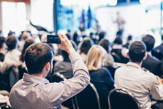 Speaker giving a talk in conference hall at business event. Rear view of unrecognizable people in audience at the conference hall. Business and entrepreneurship concept