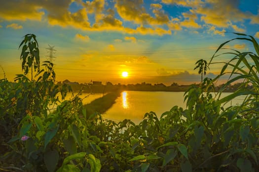 Sunset over the lake with trees and grass as foreground in Surabaya, Indonesia.