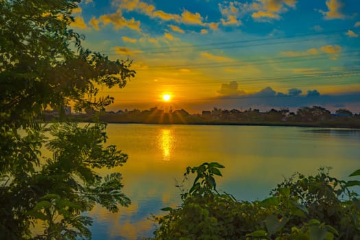 Sunset over the lake with trees and grass as foreground in Surabaya, Indonesia.