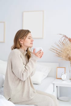 caucasian woman waking up in her bed in the morning. young millennial woman sitting on the bed in the morning drinking coffee, light and airy room