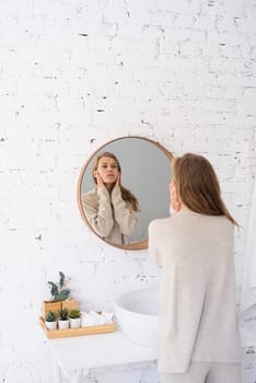 Woman looking at the mirror, making up in the morning. young millennial woman doing her morning routine at the bedroom