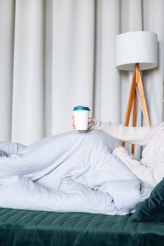 caucasian woman waking up in her bed in the morning. young millennial woman sitting on the bed in the morning drinking coffee from paper cup, mockup design