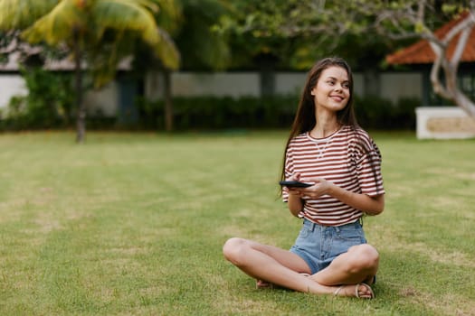 happy woman smart smiling phone grass female application lifestyle browsing girl blogger park cell striped palm outdoor tree nature shirt summer working