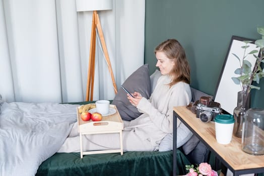 caucasian woman waking up in her bed in the morning. young millennial woman sitting on the bed in the morning drinking coffee, light and airy room