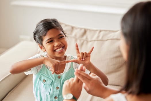 Sign language, communication and child with her mother in the living room of their family home. Happy, smile and girl kid speaking with her hands to her deaf mom to communicate in their modern house