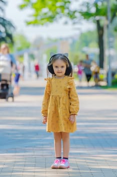 A little girl in a yellow dress stands on a street.