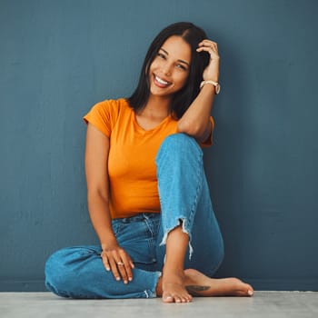 Black woman, floor and home with smile by wall for clothes, relax and fashion with barefoot. Gen z girl, model portrait and happy in house with feet, jeans and happiness on face by blue background.
