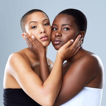 The gentle touch of the face. Portrait shot of two beautiful young women holding each others face while standing against a grey background