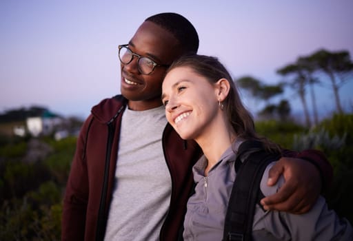 Happy couple, relax and love in an interracial relationship during sunset in the evening or night outdoors in nature. Adventure, travel and people hugging outdoors on after hiking a mountain.