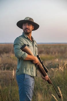 ranger in a hat stands in a field with a gun.