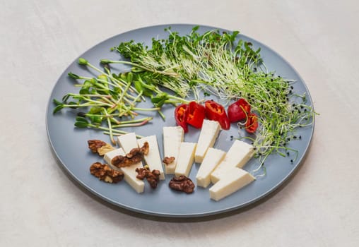 Cheese, chili peppers, walnut and micro greens on a gray plate.
