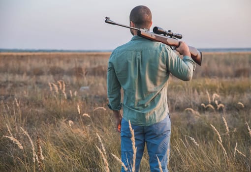 hunter stands in the field with his back putting the gun on his shoulder