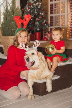 Two sisters with their dog in Christmas outfits are sitting on the porch