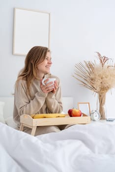 caucasian woman waking up in her bed in the morning. young millennial woman sitting on the bed in the morning drinking coffee, light and airy room