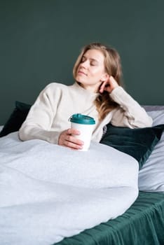 caucasian woman waking up in her bed in the morning. young millennial woman sitting on the bed in the morning drinking coffee from paper cup, mockup design