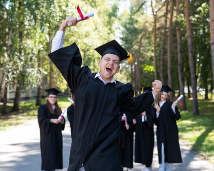 Happy young caucasian man celebrating graduation. Crowd of students graduates outdoors