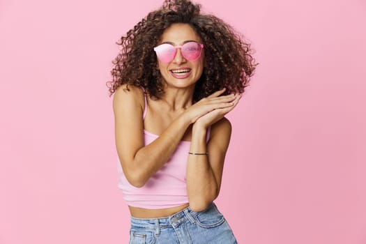 Happy woman afro curls hair dancing on a pink background in summer pink t-shirt jeans and glasses, summer vibe, copy space. High quality photo