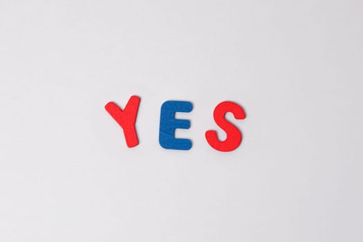 The word yes made of colored wooden letters on a light gray background. Blue and red letters form the word yes