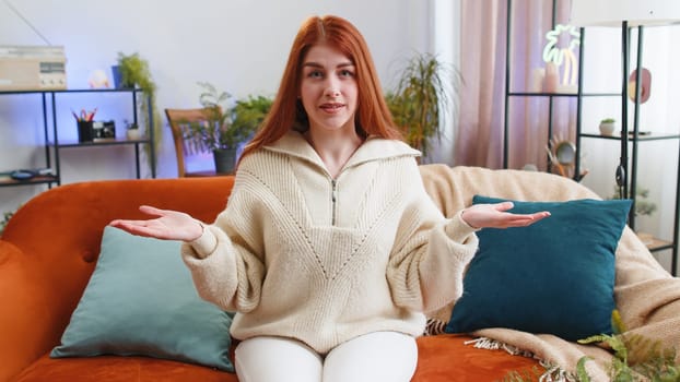 What. Why. Woman raising hands in indignant expression asking reason of failure demonstrating disbelief irritation by troubles at modern home apartment. Redhead girl in living room sitting on sofa