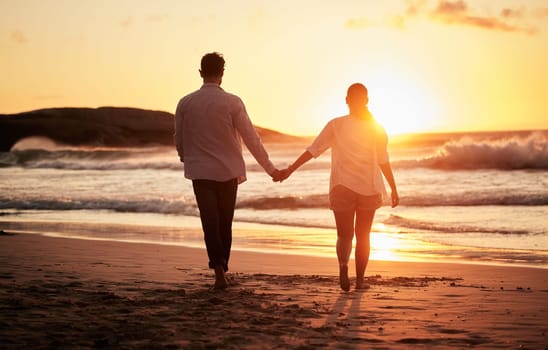 Sunset, couple holding hands and walking by the beach with a beautiful twilight. Love, romance and happy man and woman spending time together with affection by ocean, sea and sandy shore on holiday