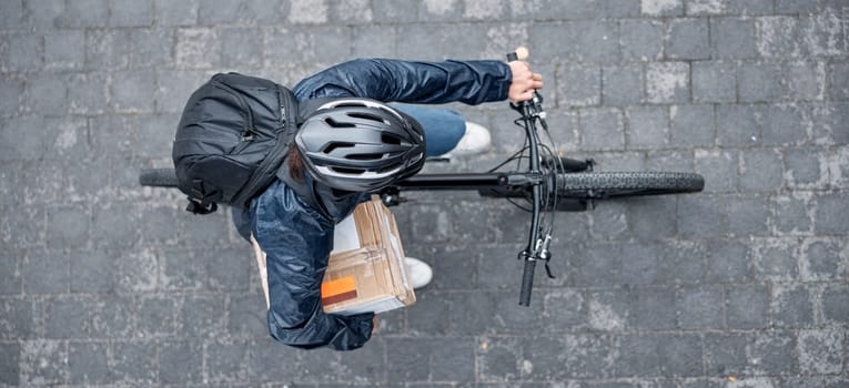 Top view, bicycle and delivery man with box in city for package, logistics and shipping. Courier, eco friendly transport and male bike driver with cargo, stock or goods for ecommerce on road in town