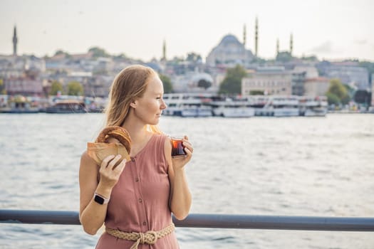 Woman in Istanbul having breakfast with Simit and a glass of Turkish tea. Glass of Turkish tea and bagel Simit against golden horn bay in Istanbul, Turkey. Turkiye.