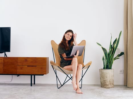 Female student study sits on a chair with a laptop work at home smile and relax, modern stylish interior Scandinavian lifestyle, copy space. High quality photo