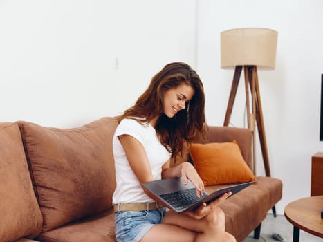 Woman freelancer sitting on the couch with a laptop beautiful smile , modern stylish interior Scandinavian lifestyle, copy space. High quality photo