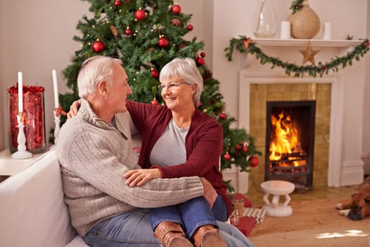 Christmas, love and senior couple on sofa in home bonding and affection. Xmas, romance and elderly, retired woman sitting on lap of man and cuddle on couch by fireplace enjoying holiday time together.