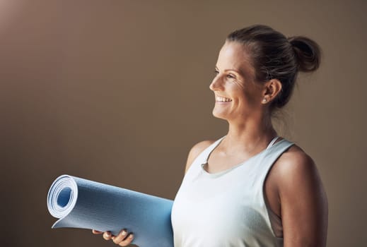 Yoga makes me happy. an attractive young woman standing alone and holding her yoga mat before an indoor yoga session