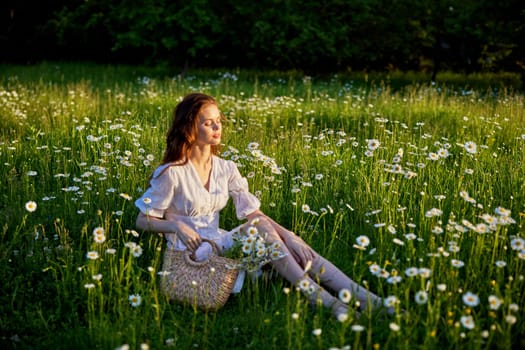 a beautiful woman in a light dress sits in a field in chamomile flowers. High quality photo