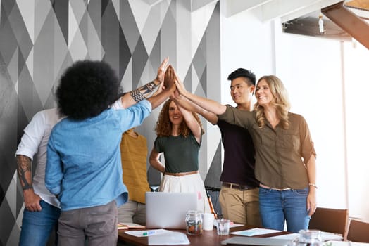 We did it again. a group of designers high fiving during having a meeting in an office