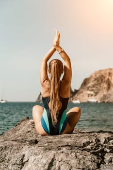 Yoga on the beach. A happy woman meditating in a yoga pose on the beach, surrounded by the ocean and rock mountains, promoting a healthy lifestyle outdoors in nature, and inspiring fitness concept