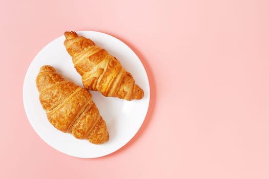 Plate with delicious croissants on a pink background. french pastries. copy space.