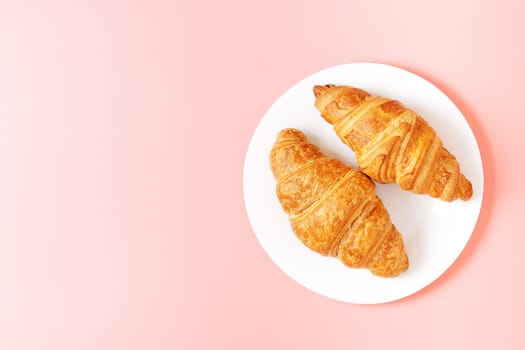 Plate with delicious croissants on a pink background. french pastries. copy space.