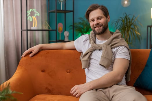 Portrait of happy calm Caucasian man at home couch smiling friendly, glad expression looking away dreaming resting, relaxation feel satisfied concept good news, celebrate win. Young guy in living room