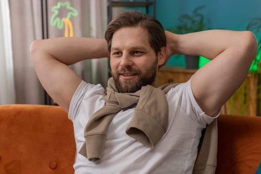Tired man lying down on comfortable couch, taking a rest, daytime nap. Portrait of smiling Caucasian guy holding hands behind head relaxing, falling asleep at home apartment living room on sofa