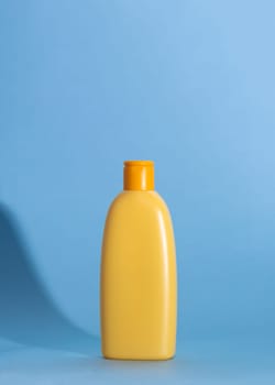 Mock up of a yellow bottle with children's cosmetics on a blue background. Hard shadows, copy space.