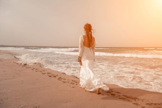 woman sea white dress. Model in boho style in a white long dress and silver jewelry on the beach. Her hair is braided, and there are many bracelets on her arms