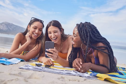 Girl friends, ocean fun and phone of a teenager laughing at funny meme by the sea in Miami. Travel, vacation and sunshine with happy students enjoying spring break with mobile app lying on sand.