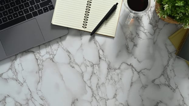 Feminine workspace with laptop, notepad and coffee cup on marble table. Top view with copy space.