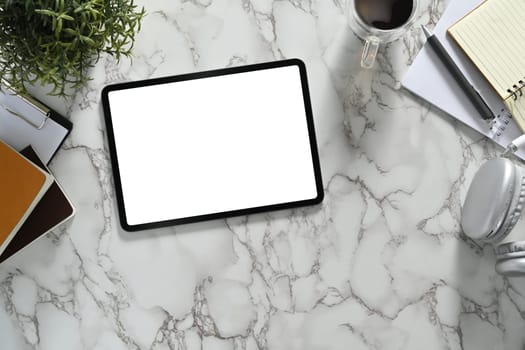 Top view of digital tablet with white empty screen, headphone and coffee cup on marble background.