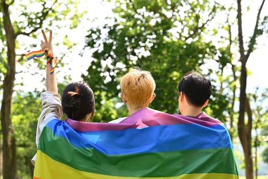 Young people with LGBTQ pride flag, enjoy outdoor activities at nature park. LGBT community, homosexual and equal rights.