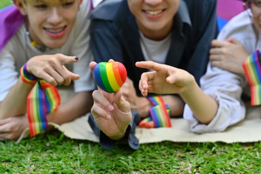 Group of young people wearing rainbow awareness wristbands, enjoying outdoor activities at public park. LGBTQ community concept.