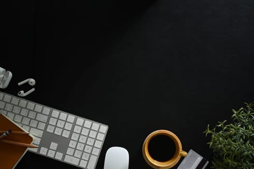 Flat lay, top view of keyboard, coffee cup, notepad and earphones on black leather background.