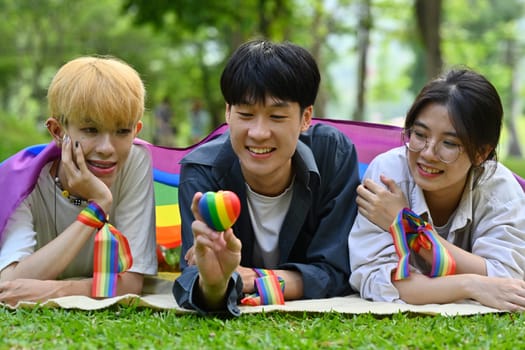 Group of young people wearing rainbow awareness wristbands, enjoying outdoor activities at public park. LGBTQ community concept.