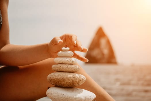 Woman bilds stones pyramid on the seashore on a sunny day on the blue sea background. Happy holidays. Pebble beach, calm sea, travel destination. Concept of happy vacation on the sea, meditation, spa