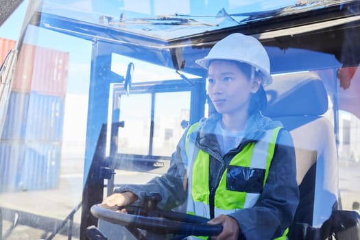 Asian woman, logistics and machine for industry shipping at work for transportation in container yard. An engineer working in industrial warehouse with transport machinery for cargo shipment.