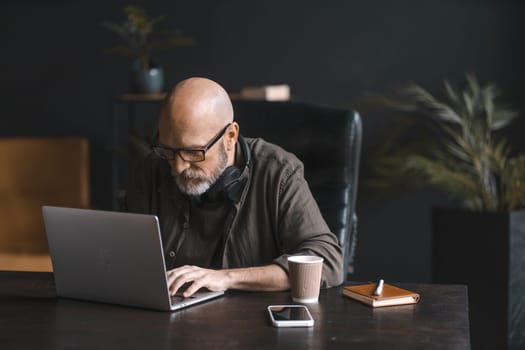Hard worker concept, dedicated mid-aged man spends day immersed in work, diligently operating laptop with focus and determination. Commitment to job showcases professionalism and drive for success. High quality photo