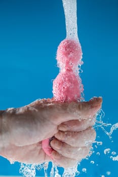 Woman holding pink anal beads under running water on blue background. Sex toy hygiene concept